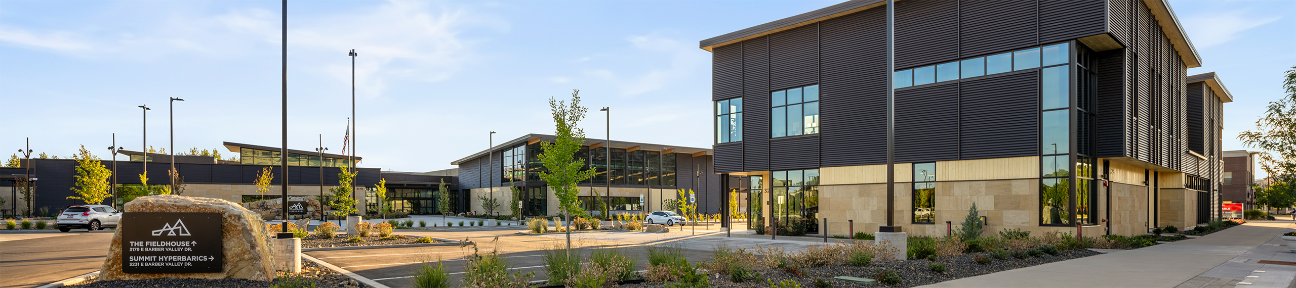 Summit Hyperbarics & Wellness building alongside the Idaho Outdoor Fieldhouse, featuring modern architecture, large windows, and a landscaped parking area with signage.