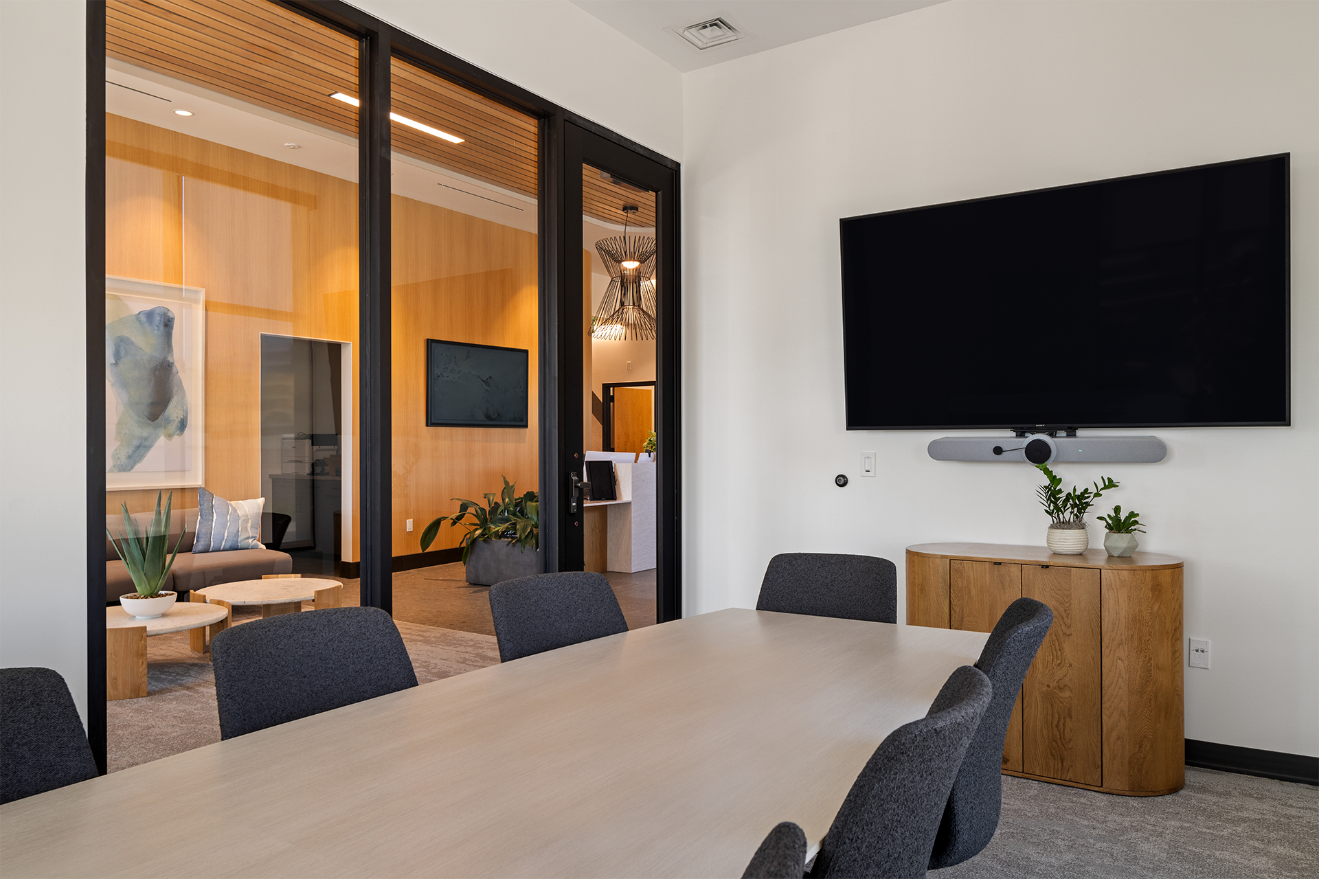 Conference room with a large screen, modern decor, and glass walls opening into a lounge area.