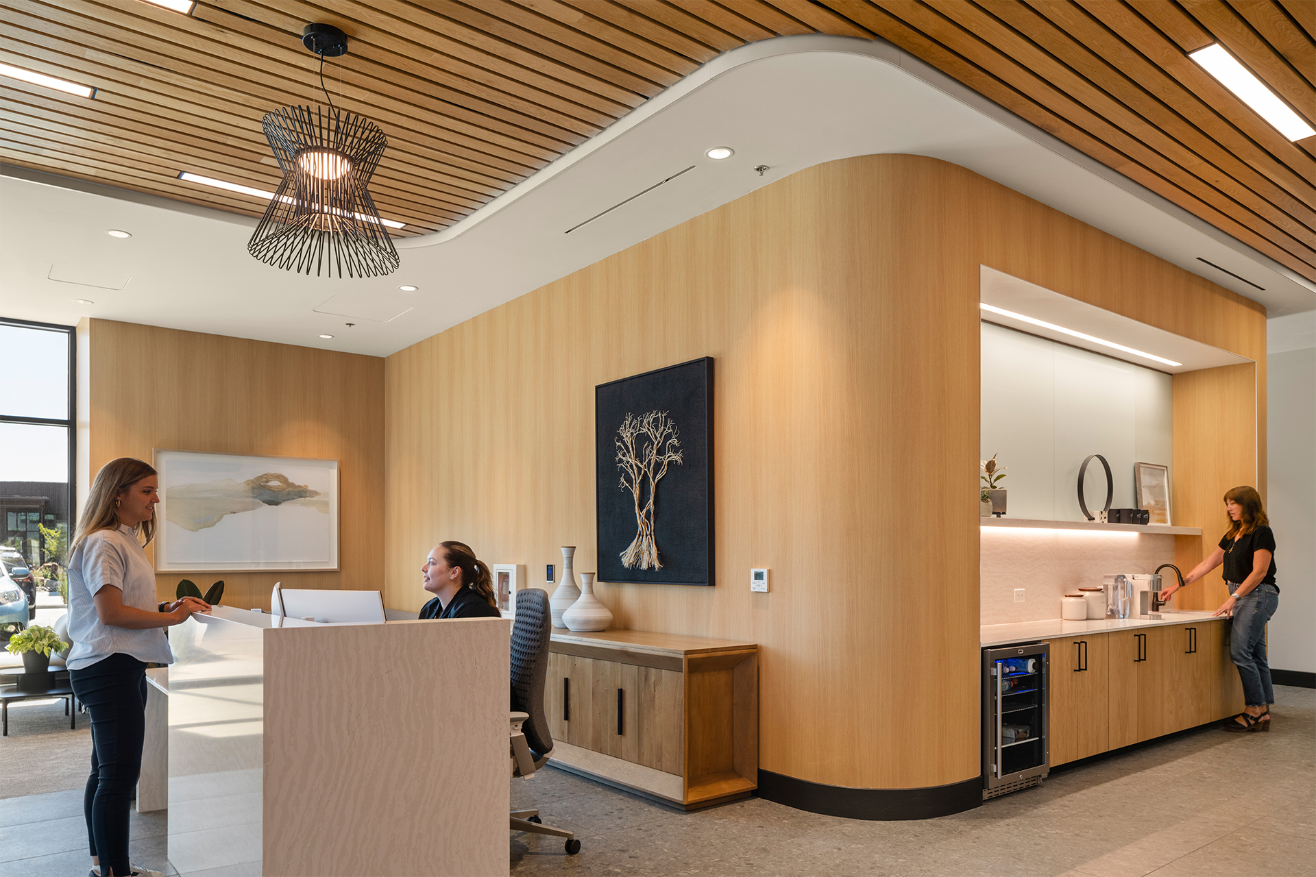 A client speaking with a receptionist at the Summit Hyperbarics & Wellness first-floor lobby, featuring modern wood paneling, a beverage station, and warm lighting.