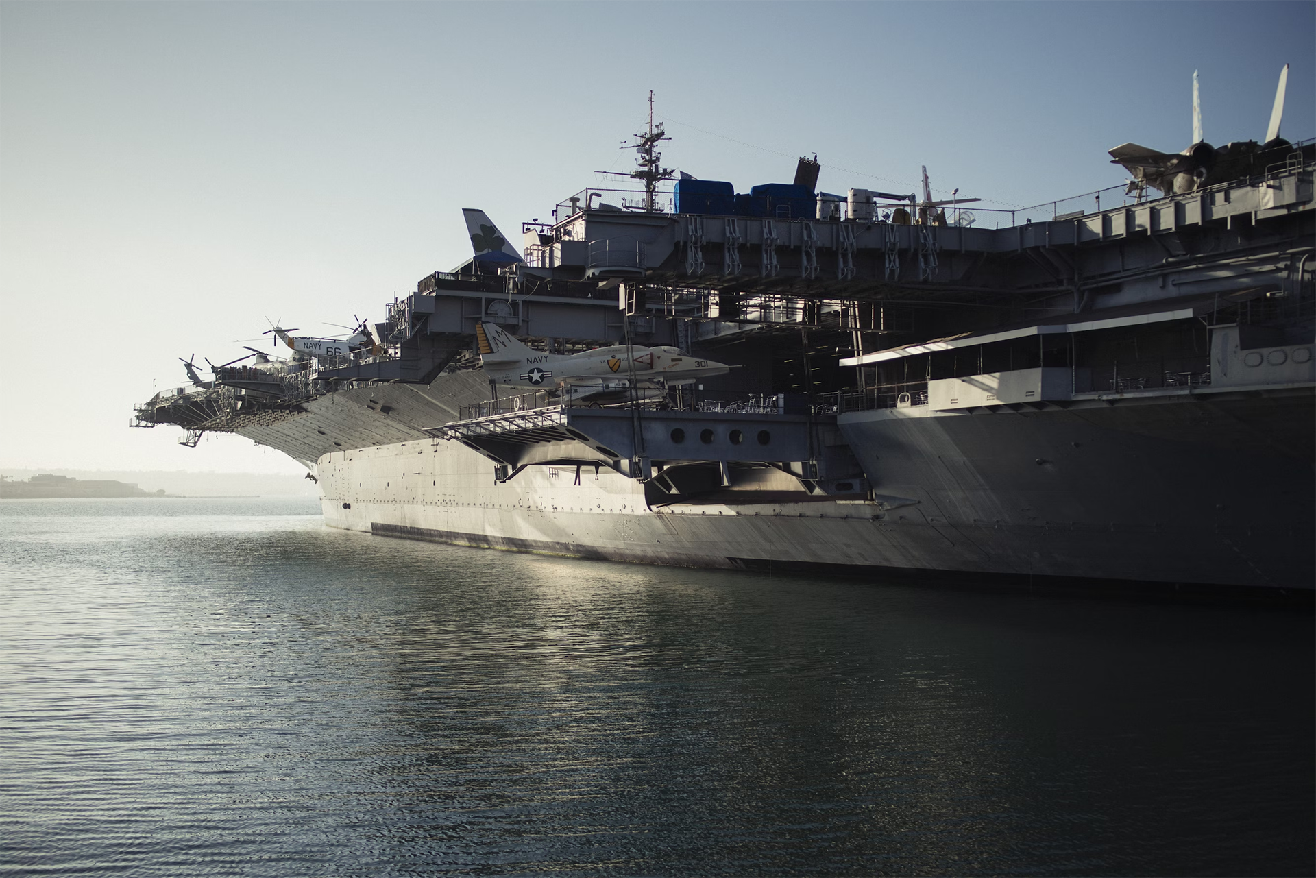 A large U.S. Navy aircraft carrier docked in calm waters, with fighter jets and helicopters on the deck.